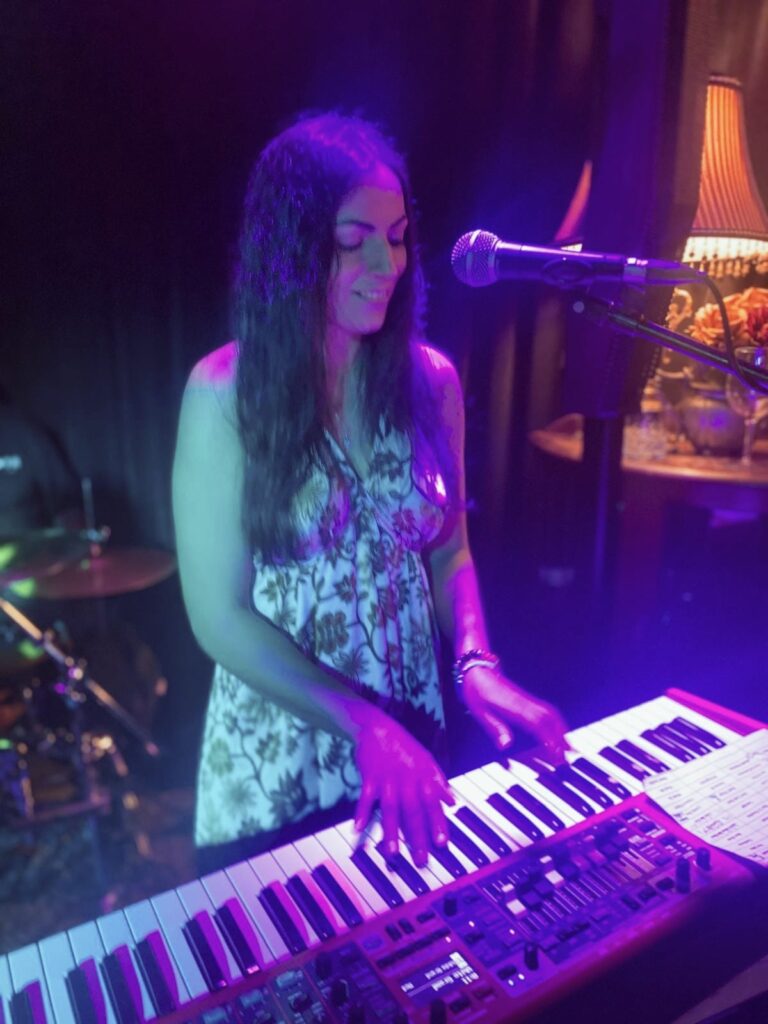 Colleen singing and playing keyboard on stage under purple lights